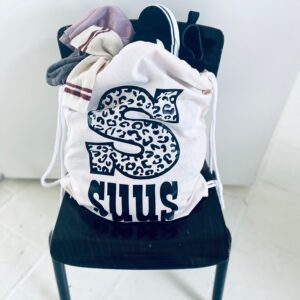 Witte gymtas met luipaard S-logo gevuld met kleding op zwarte stoel in Zeeuwse cadeauwinkel