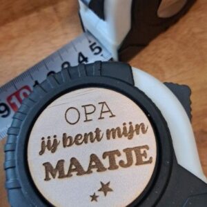 Houten medaille met tekst 'OPA jij bent mijn MAATJE' en rolmaat op houten tafel