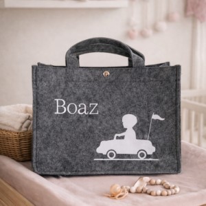 Grijze vilten speelgoedtas met naam Boaz en auto-opdruk in babykamer met knuffels op achtergrond
