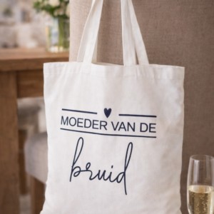 Witte canvas tas met opschrift 'Moeder van de bruid' hangend over beige stoel als cadeau-idee