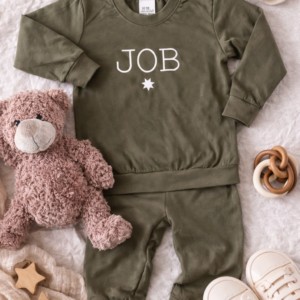 Olijfgroen babypakje met naam JOB, omringd door knuffel, sokjes en houten speelgoed op lichte achtergrond