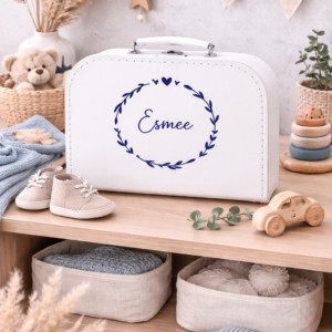 Wit koffertje met naam Esmee en blauwe krans, gepersonaliseerd kraamcadeau tussen babyspeelgoed en decoratie