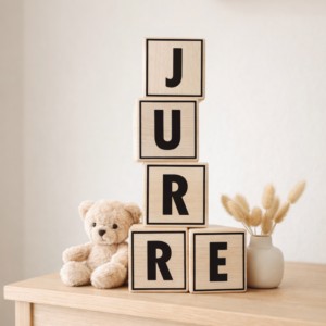Houten letterbblokken spelling 'JURRE' met teddybeer en droogbloemen op houten ladekast
