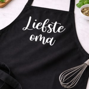 Zwart keukenschort met witte tekst 'Liefste oma', ideaal cadeau voor oma met kookgerei en ingrediënten