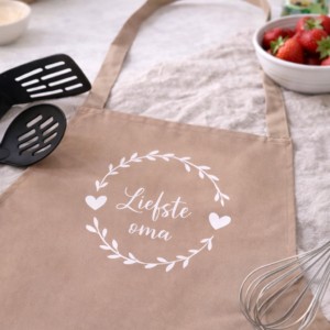 Beige keukenschort met tekst 'Liefste oma' en bloemenkrans, ideaal cadeau voor oma