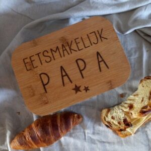 Houten ontbijtplankje met tekst 'Eetsmakelijk PAPA' op linnen doek met croissant en broodjes
